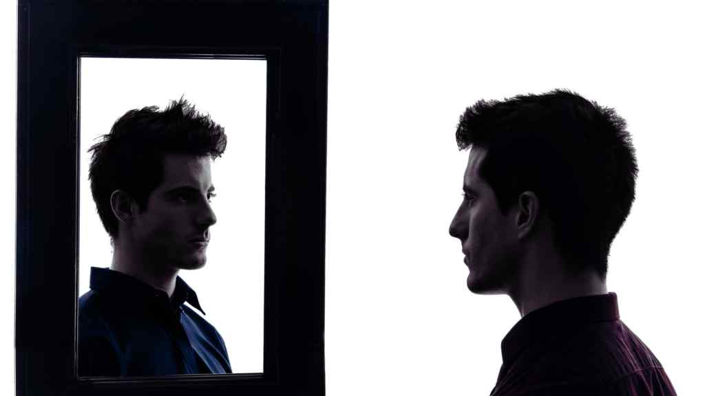 Silhouette of a man gazing at his reflection in a mirror. The background is white, highlighting the profile and creating a contemplative tone.